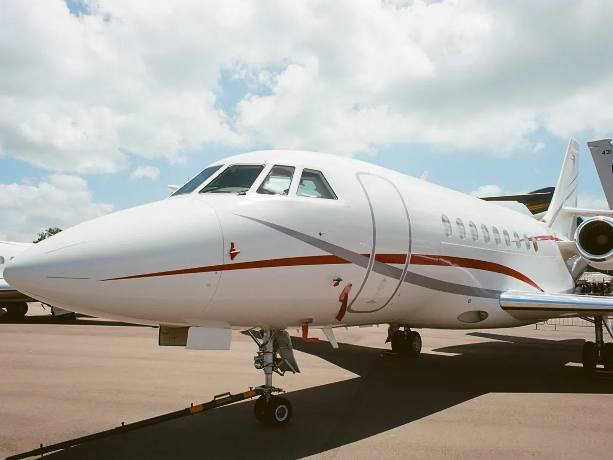 Nose of a white business jet with a red stripe on a sunny ramp